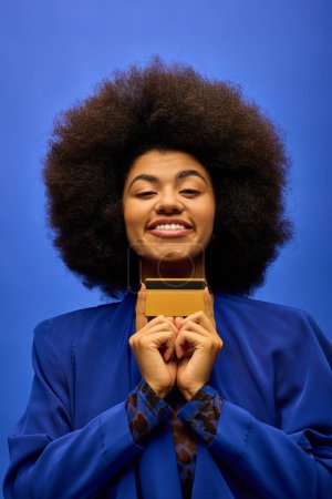 Trendy African American woman with curly hairdohair, holding credit card.