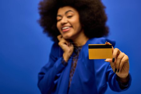 Joyful African American woman in stylish attire holding a credit card and smiling.