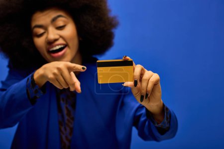Stilvolle Afroamerikanerin in trendiger Kleidung zeigt auf eine Kreditkarte.