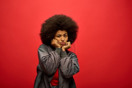 Stylish African American woman in trendy attire posing in front of a vibrant red backdrop.