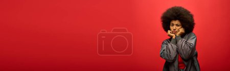 Photo for Stylish African American woman with curly hairdostanding confidently against bright red background. - Royalty Free Image