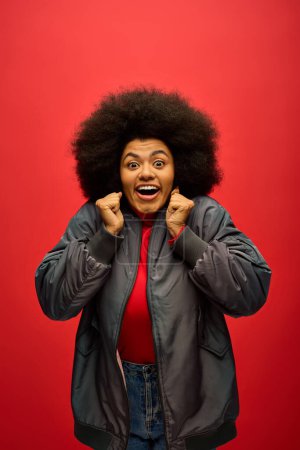 Photo for Stylish African American woman with curly hairdoposes confidently in front of a striking red backdrop. - Royalty Free Image
