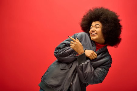 Trendige Afroamerikanerin mit lockigem Haar posiert vor leuchtend rotem Hintergrund.