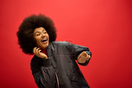 Afroamerikanerin mit beeindruckender Afro-Frisur steht selbstbewusst vor fettem roten Hintergrund.
