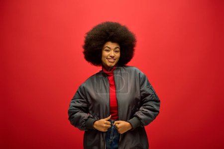 Photo for African american woman with curly hairdostands confidently in front of a bold red background. - Royalty Free Image