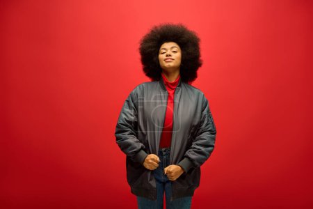 Téléchargez les photos : Femme afro-américaine aux cheveux bouclés se tient en toute confiance devant un fond rouge vibrant. - en image libre de droit