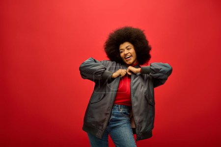 Stylish African American woman with curly hairdohair standing confidently against a striking red background.