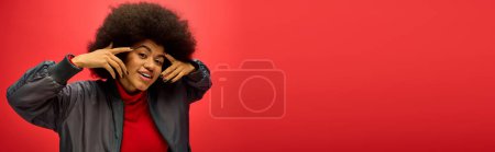 A stylish woman with curly hairdoposing actively on red backdrop.