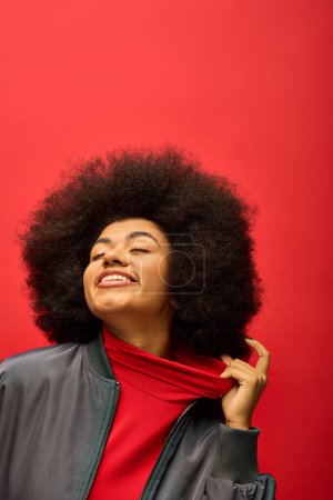 Téléchargez les photos : Une femme afro-américaine branchée pose dans un cadre vibrant, portant une chemise rouge et une veste noire. - en image libre de droit