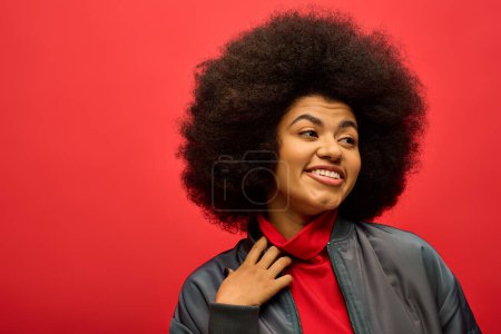 Photo for Stylish African American woman with curly hairdo wearing red shirt poses against vibrant backdrop. - Royalty Free Image