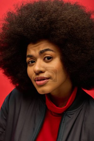 Trendy African American woman with curly hairdo poses confidently in a bright red shirt.