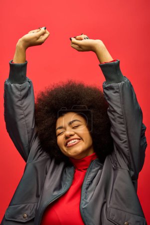 Foto de Mujer afroamericana con estilo en traje de moda con cabello rizado, levantando brazos en un entorno vibrante. - Imagen libre de derechos