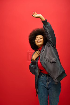 Stilvolle Afroamerikanerin posiert in trendiger Kleidung vor fettem roten Hintergrund.