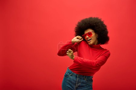 Téléchargez les photos : Une femme afro-américaine élégante dans une chemise rouge et des lunettes de soleil posant sur un fond vibrant. - en image libre de droit