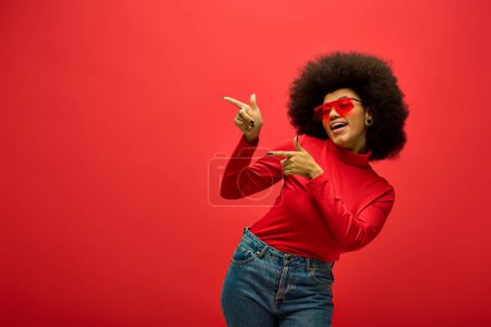 Stylish African American woman striking a pose in trendy red shirt and sunglasses.