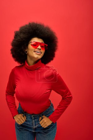 Stylish African American woman in red glasses and shirt posing on vibrant backdrop.