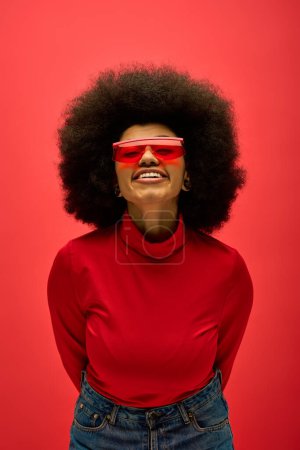 Stylish African American woman in red glasses and shirt posing on vibrant backdrop.
