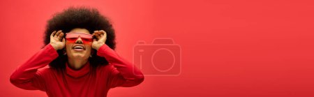 Mujer afroamericana luce con confianza una camisa roja y gafas a juego.
