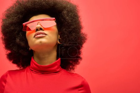 A fashionable African American woman poses in red glasses and shirt against a vibrant backdrop.