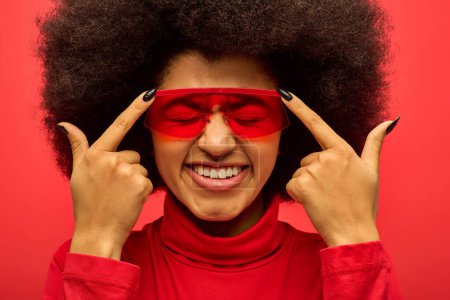 Stylische Afroamerikanerin mit roten Eyelinern und Augenbinde vor lebendigem Hintergrund.