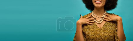 Fashionable African American woman with curly hairdo posing on vibrant blue backdrop.