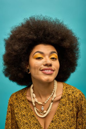 An African American woman with a striking afro and yellow makeup poses stylishly on a vibrant backdrop.