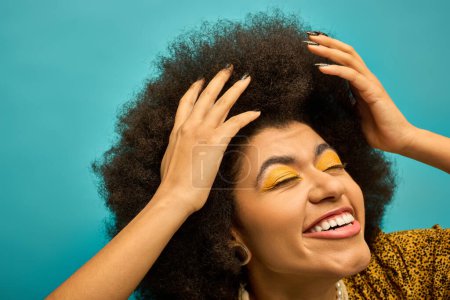 A stylish African American woman with bright yellow eye shadow poses on a vibrant backdrop.