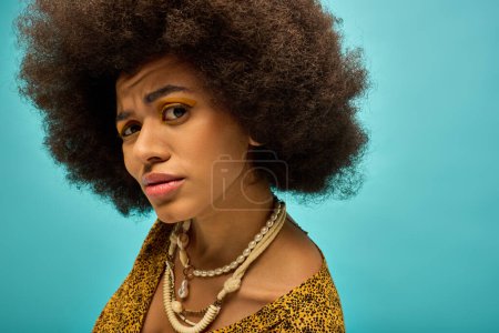 Trendy African American woman with curly hairdoposes in stylish attire against vibrant backdrop.