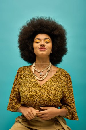 Téléchargez les photos : Femme afro-américaine élégante avec coiffure bouclée sur une chaise en tenue tendance sur un fond vibrant. - en image libre de droit
