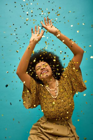 Young African American woman in stylish attire raises hands, surrounded by colorful confetti.