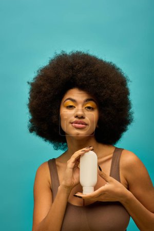 Téléchargez les photos : Femme afro-américaine élégante avec des cheveux bouclés tient une bouteille sur fond vibrant. - en image libre de droit