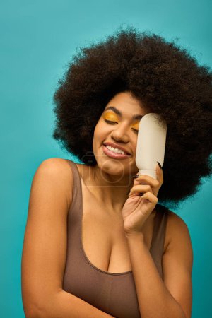Stylish African American woman with trendy attire holding brush to her face.