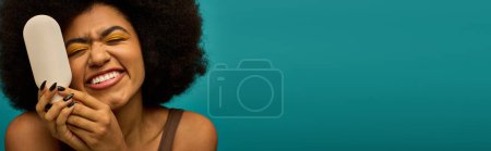 Photo for Stylish African American woman holding a brush to her face with vibrant backdrop. - Royalty Free Image