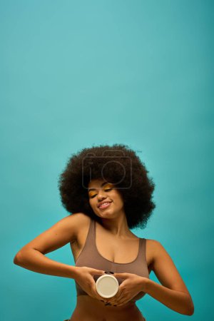 Stylish African American woman with curly hairdohair holding cream against a vibrant backdrop.