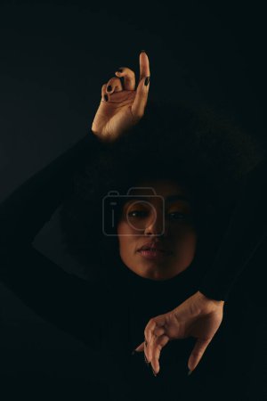 Mujer afroamericana de moda levantando alegremente su mano contra el colorido telón de fondo.