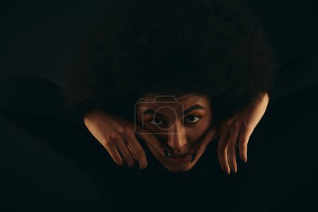 Eine stylische Afroamerikanerin in trendiger Kleidung, die ihr Gesicht mit den Händen bedeckt.