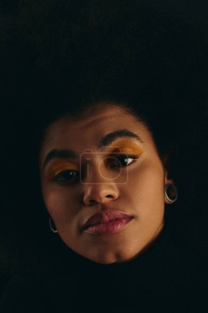 Foto de Un primer plano de una elegante mujer afroamericana con un voluminoso peinado afro sobre un vibrante telón de fondo. - Imagen libre de derechos