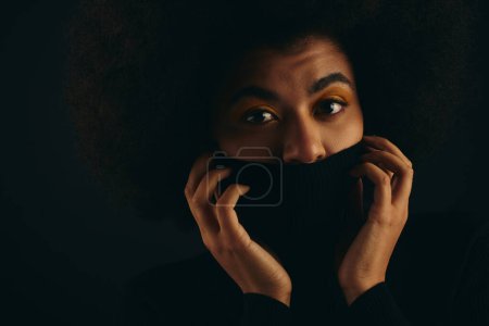 Afroamerikanerin bedeckt Gesicht stilvoll mit schwarzem Tuch vor lebendigem Hintergrund.