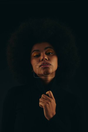 Téléchargez les photos : Femme afro-américaine à la mode avec cheveux bouclés debout dans l'obscurité. - en image libre de droit