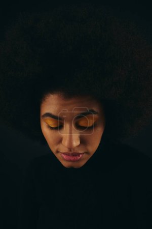 A stylish African American woman with curly hairdolooks down at her cell phone.