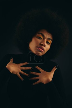 Stylish African American woman in trendy attire holding her hands on her chest in peaceful gesture.