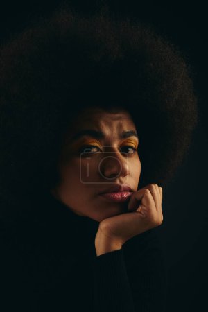 Stilvolle Afroamerikanerin mit lockigem Haar posiert vor lebendigem Hintergrund.