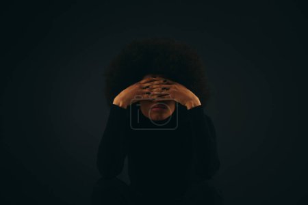 Foto de Una mujer afroamericana con estilo en traje de moda cubre su cara con sus manos. - Imagen libre de derechos