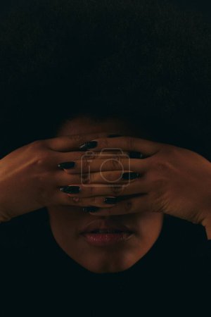 Una mujer afroamericana con estilo en traje de moda cubre su cara con sus manos.