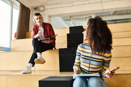 Un hombre y una mujer, ambos estudiantes, participan en una conversación mientras están sentados en los escalones interiores de una universidad