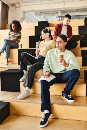 Téléchargez les photos : Groupe d'étudiants multiculturels, dont une afro-américaine, assis ensemble sur un escalier à l'intérieur - en image libre de droit