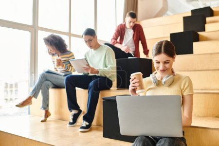 Multikulturelle Gruppe junger Leute, die auf Treppen sitzen, sich auf Laptops konzentrieren und sich mit digitalem Lernen beschäftigen
