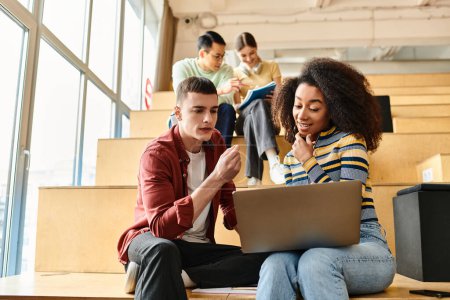 Multikulturelle Gruppe junger Studenten, die auf den Stufen eines Gebäudes sitzen und sich auf den Laptop-Bildschirm konzentrieren