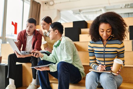 Téléchargez les photos : Groupe multiculturel d'étudiants s'engagent dans le travail de groupe sur les ordinateurs portables tout en étant assis sur les marches - en image libre de droit