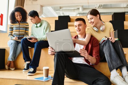 Foto de Los estudiantes multiculturales se sientan en los escalones, absorbidos en computadoras portátiles con fines educativos. - Imagen libre de derechos